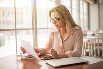 Young businesswoman in eyeglasses in cafe sitting reading documents concentrated