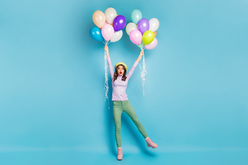 Full size photo of crazy pretty lady hold many air balloons arms raising up wind blowing wear purple jumper beret cap green trousers boots isolated blue color background