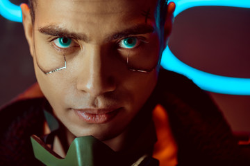 handsome and bi-racial cyberpunk player looking at camera near neon lighting