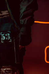 cropped view of cyberpunk player with gun on black with neon lighting