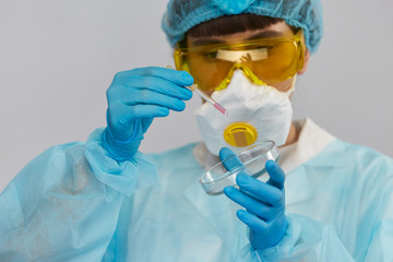female biologist in protactive suit and glasses leaving samples with pipette