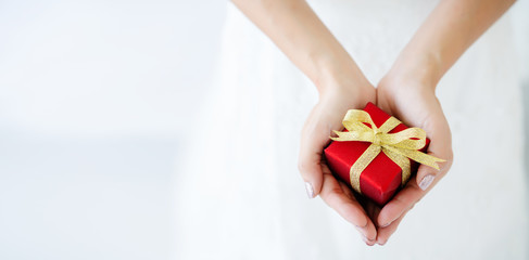 Red gift box with a golden bow tied on a woman's hand. Business Online delivery concepts