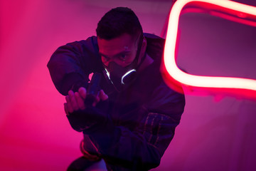 overhead view of armed bi-racial cyberpunk player in mask holding gun near neon lighting