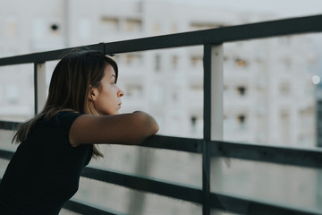 Young sad woman looking outside through balcony of an apartment building