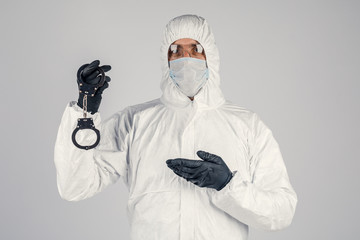 Fototapeta na wymiar A man in a white chemical protective suit with handcuffs in his hands. An epidemic pandemic is a new rapidly spreading virus, a medical concept. Lack of freedom during the virus.