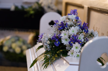 Modest flower arrangement on a white coffin cover next to wall with Bible texts in small Lutheran...