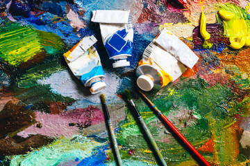 texture of bright colors on a palette with brushes and empty tubes, artist concept