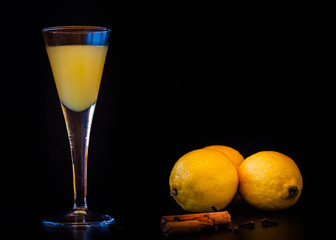 Limoncello in elegant liquor glass with lemon, cinnamon and cloves on dark background. Sicilian lemon liquor. 