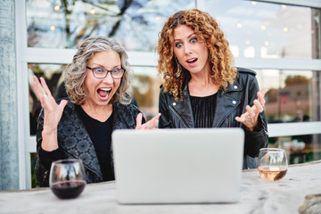 Two women looking at a laptop computer and being surprised 