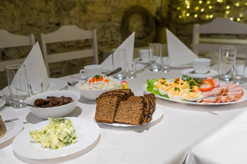 Festive table setup, white napkins set  triangularly, elegant simple tableware on long table. Salad, black bread and spicy butter. Modest dinner with few close people.