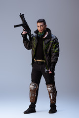 handsome mixed race cyberpunk player holding gun while standing on grey