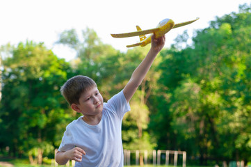 Young boy playing with toy glider in park on summer day at sunset.