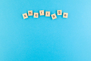 Obraz premium The inscription Shortage laid out of wooden cubes on a blue background.