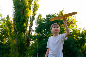 Young boy playing with toy glider in park on summer day at sunset.