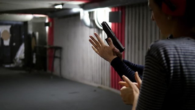 Rear view of a girl aiming at a target in a shooting gallery, holding a gun in her hands