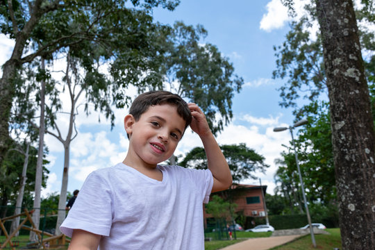 6 year old child outdoors, with a shy smile and running his hand through his hair.