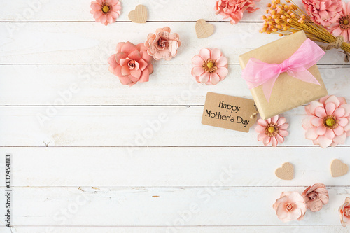 Happy Mothers Day corner border with paper flowers, gift box and tag. Top view over a white wood background. Copy space.
