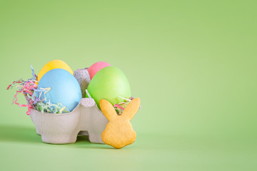 Colored Easter eggs in a carton and bunny-shaped cookies. on a green background. Place for text.