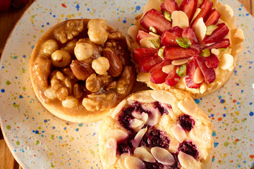 Three mini tarts cupcakes with strawberries, walnuts, almond, nuts and blueberries on plate. Top view