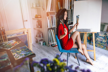 artist girl in a red dress sitting on a chair in the studio
