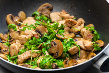 turkey meat with mushrooms and rocket in frying pan