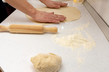 Roll out the dough. baker rolls out the dough on a wooden kitchen table sprinkled with flour