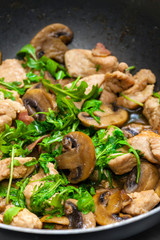turkey meat with mushrooms and rocket in frying pan