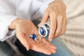 Female hand close up holding a medicine, elderly woman hands with pill on spilling pills out of bottle.