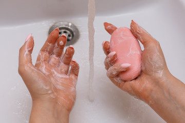 A girl washes her hands over a sink with antibacterial soap for prevention against covid-19. Close up of female hands and soap.