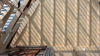 Sunlight and shadow on surface of white wooden roof truss structure with construction material on top of house building site
