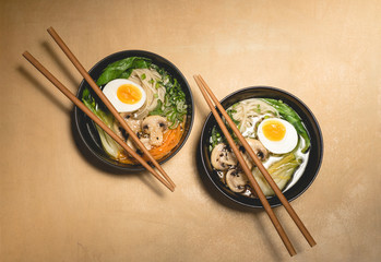 Traditional japanese Ramen soup with  mushrooms, Bok Choy, greens in  two black bowls on the orange background, top view, close up. Japanese cuisine concept