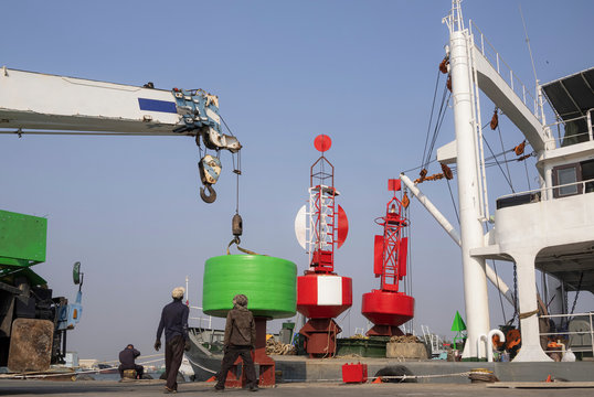 Asian Workers Group With Crane Truck Are Working To Transfer Green Lateral With Red Fairway Buoys And Large Concrete Anchor Block Into The Ship For Traffic Sign Installation In The Sea.