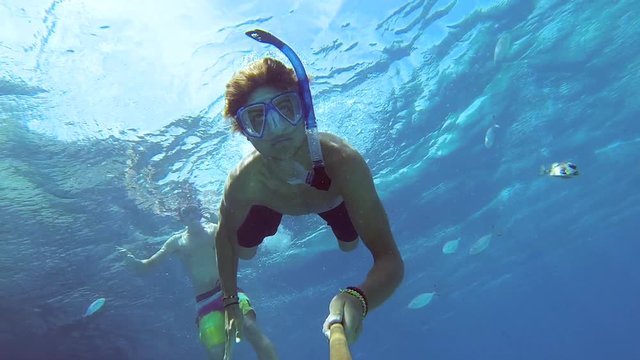 Selfie shot of a young man snorkeling and diving underwater in a blue ocean with a lot of fish around him