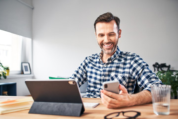 Smiling freelancer checking his smartphone while working from home office
