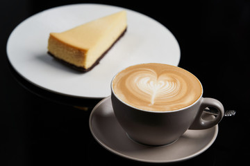 Cup of tea and slice of cheesecake on white plate on table