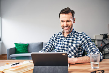 Portrait of smiling man working from home looking at digital tablet