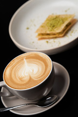 Cappuccino coffee cup and cake on plate on table, close-up.