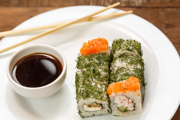 Set of rolls with dill and salmon on a white plate with soy sauce.