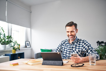 Smiling freelancer working from home sitting at a desk with digital tablet and smartphone