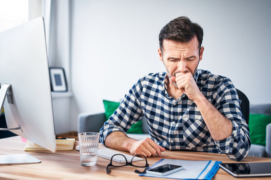 Man coughing while working on a computer from home