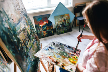 Girl artist paints an oil painting on canvas. Brush dips into the palette