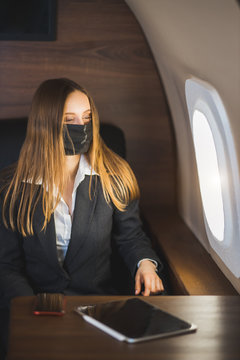 Young beautiful business woman sitting on a plane in a black medical mask during a coronavirus pandemic
