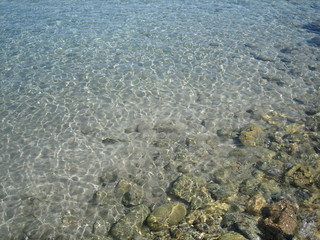 Through the clear water in the rays of the reflection of the sun, you can see the shallow sea floor of sand, pebbles and stones of a gray brown color.