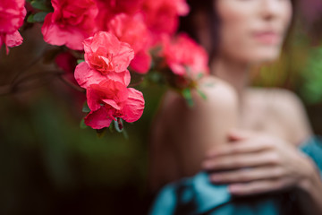 Beautiful romantic young woman in a greenhouse with azaleas. Focus on the azalea flower. The girl's face is blurry in the background. Art portrait.