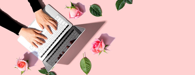 Woman using her laptop with pink roses - flat lay