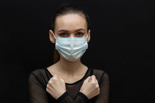 Beautiful girl in a protective mask and with a syringe in her hand. Protect yourself from the virus. Black clothes and background. Protection.