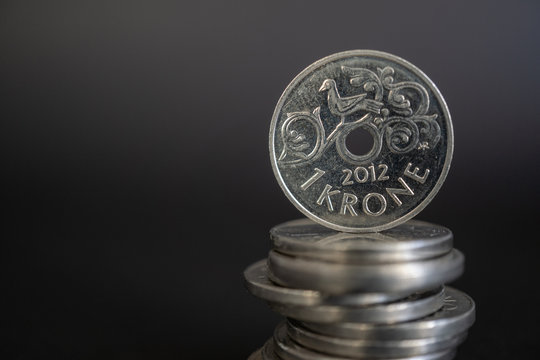 Close-up shot of norwegian one krone coin standing on stack of coins against black background. Economy of Norway.