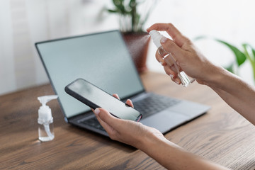 Woman disinfect smartphone screen, sitting near laptop at home