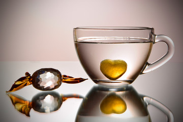 A bowl with a heart filled with liquid with a glass candy.