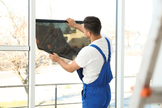 Professional worker tinting window with foil indoors